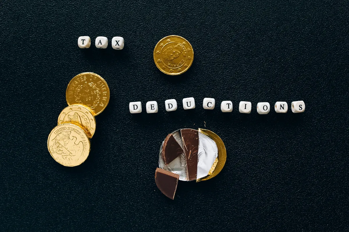 Creative concept of tax deductions using chocolate coins and letter tiles on a black background.