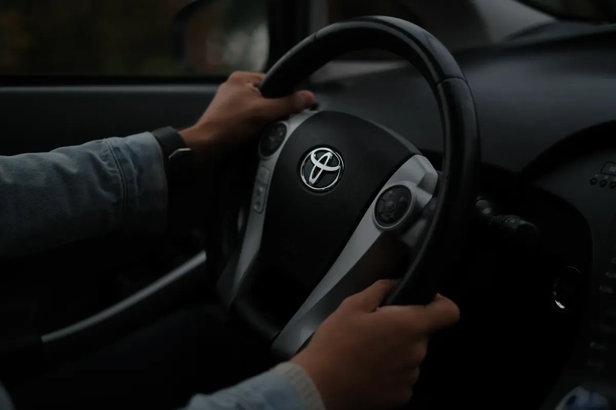 車のステアリングホイールに手が置かれた様子、車内からのクローズアップ。暗いムード。