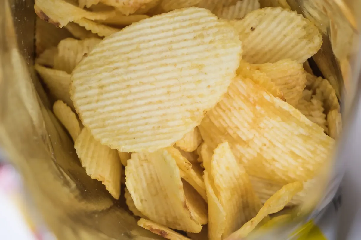 A detailed look at crispy ridged potato chips in an open snack bag, highlighting flavor and texture.