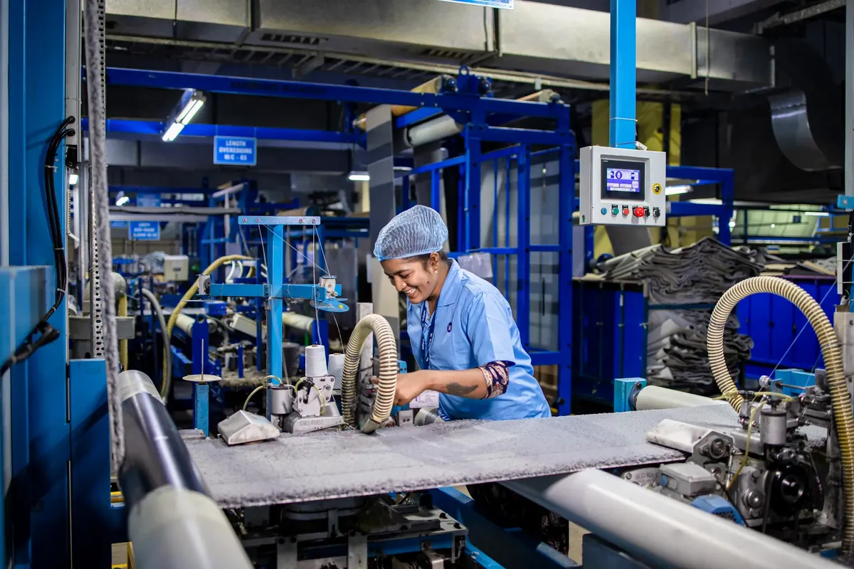 Indian female factory worker smiling while operating complex textile machinery in an industrial setting.